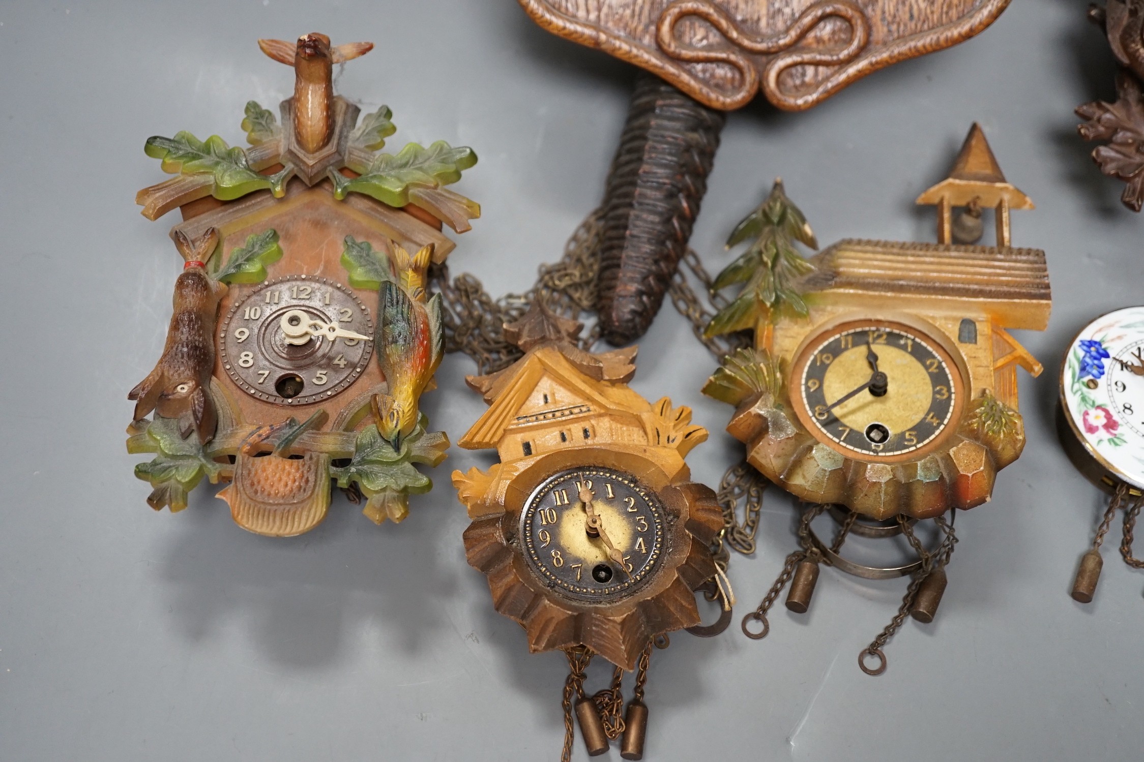 An early 20th century German Jugendstil oak wall timepiece, four miniature Black Forest timepieces and three floral enamelled examples, largest 23cms high